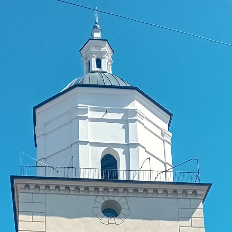 La partie supérieure de l'église du Martyre de Saint Jean-Baptiste à Sambor, avec une tour octogonale blanche et un dôme sur fond de ciel bleu clair.