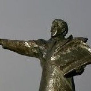 Bronze statue of Paweł Edmund Strzelecki in Jindabyne, Australia, depicting him with an outstretched arm and holding a map, against a clear sky.
