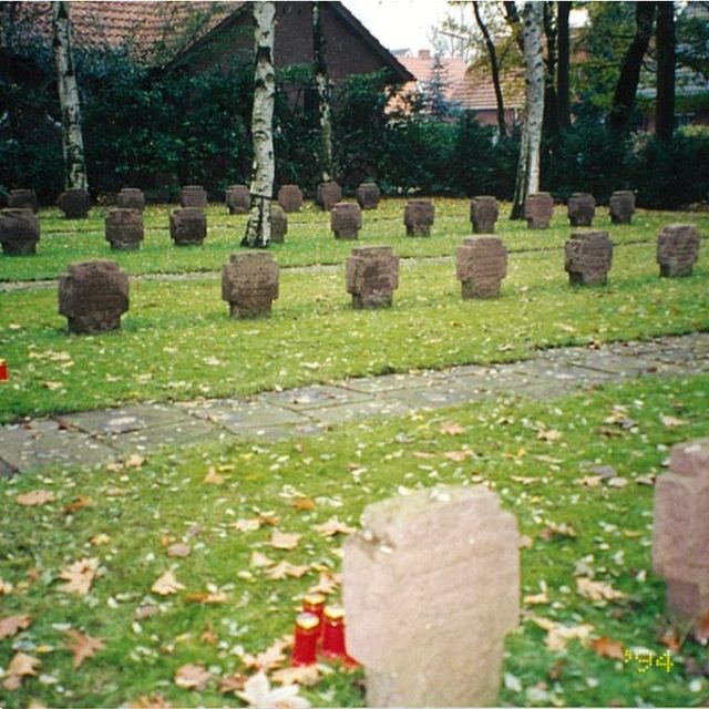 Pierres tombales sur une zone herbeuse du nouveau cimetière, entourée d'arbres. Chaque pierre est rectangulaire et des bougies rouges sont placées près de certaines.