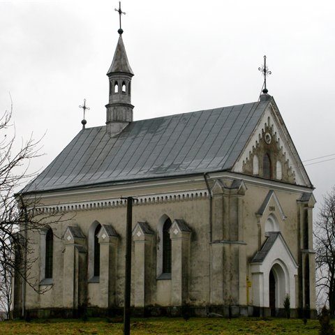 Église Saint-Michel Archange à Mościska-Zakościele avec une façade simple, un pignon triangulaire, des fenêtres en arc brisé et un toit en métal surmonté d'une croix.