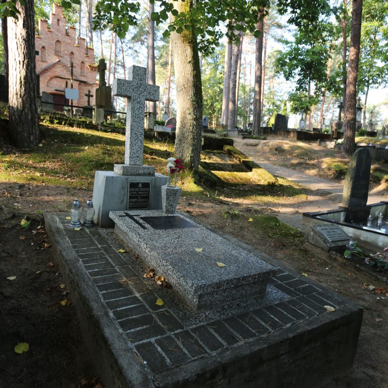 Tombe de Wacław et Adam Sikorski avec une croix en terrazzo sur une base en béton, plaque d'inscription en zinc et plaque en granit noir. Entourée d'arbres et d'autres tombes dans un cimetière.