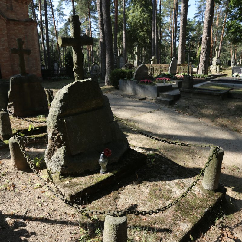 Nagrobek z krzyżem w formie pnia drzewa na granitowym głazie, otoczony czterema różowymi granitowymi słupkami z żelaznymi łańcuchami. Na głazie wykuta tablica inskrypcyjna.