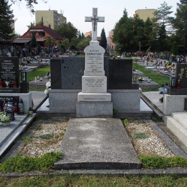 Tombe des familles Gemrotova et Dřizg avec une pierre tombale ornée d'une croix sur un piédestal à trois niveaux. La croix a des bords biseautés et une petite croix en métal avec le Christ à l'intersection. Inscriptions gravées sur chaque niveau.