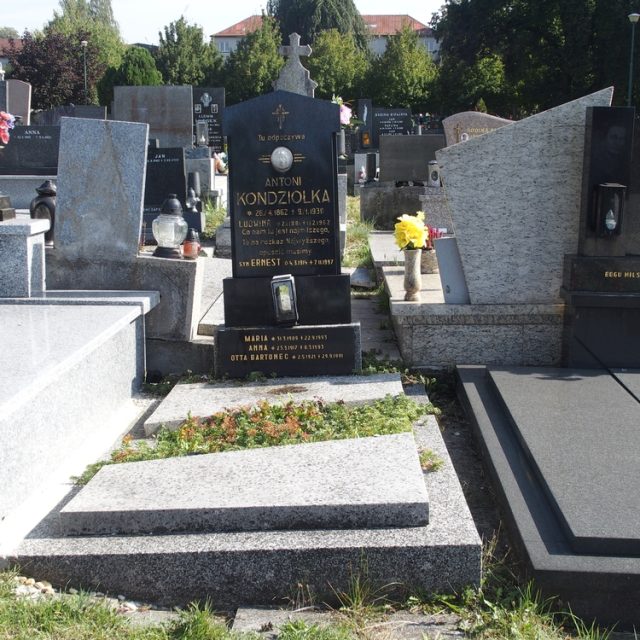 Pierre tombale de la famille Kondziołka et Otta Bartoniec avec une croix et un relief céramique de la tête du Christ. Lanterne en métal et plaques gravées présentes. Entouré d'une bande avec deux plaques et une jardinière.