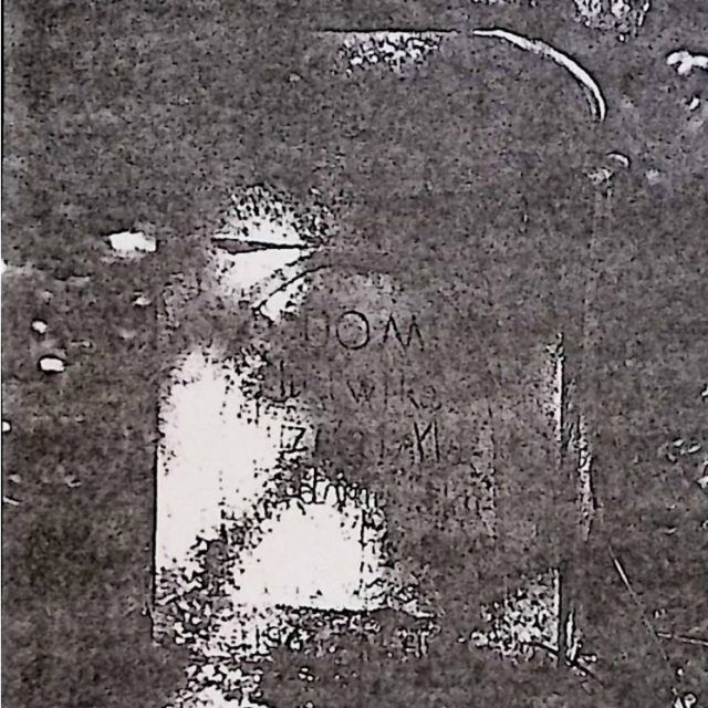 Tombstone with a cross on a pedestal, featuring a rectangular plate with engraved inscription. The base is flat, the shaft has a semicircular front panel, and the top is profiled with beveled corners.