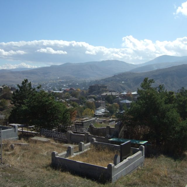 Vue du cimetière arménien à Akhaltsikhe, entouré d'arbres et de tombes en pierre, avec en arrière-plan des collines et des maisons dispersées sous un ciel nuageux.