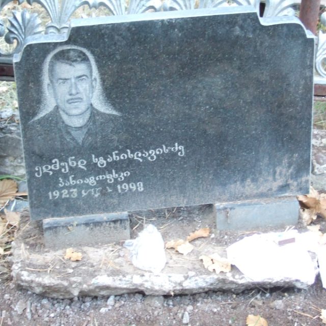 Pierre tombale en marbre noir avec un portrait gravé et une inscription dans un script étranger, entourée de feuilles tombées. Partie d'une enceinte partagée avec d'autres tombes de la famille Poniatowski.