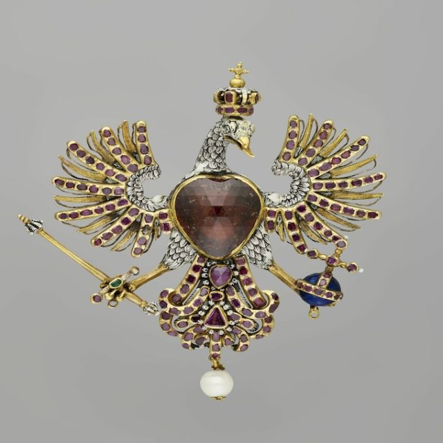 Broche en forme d'aigle en or avec un grand grenat sur la poitrine, rubis sur les ailes et la queue, tenant un sceptre et un orbe. Tête couronnée avec détails en émail, perle suspendue à la queue.