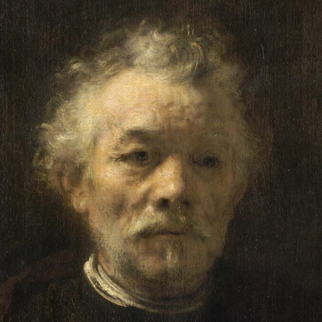 Portrait d'un homme âgé avec des cheveux gris courts et bouclés, une barbe taillée et une moustache. Il porte un manteau brun avec un col et une chemise blanche. Le fond est sombre et neutre.