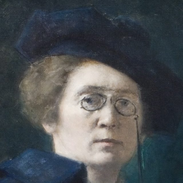 Autoportrait de Maria Dulębianka datant d'environ 1905. L'artiste porte un béret et un manteau bleu marine ; elle a les cheveux courts et porte des lunettes à double verres. Son visage arbore une expression sérieuse sur un fond sombre.
