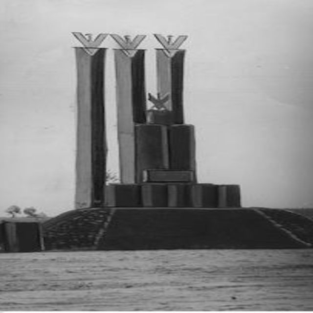 Monument commémorant la construction de la route Pinsk-Kobrin, composé de trois grands piliers surmontés d'aigles stylisés et d'un pilier inférieur avec un aigle, le tout posé sur une base à gradins avec une plaque d'inscription.