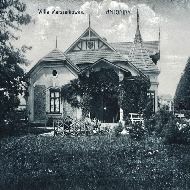 Historyczna fotografia willi Marszałkówka w Antoninach, zbudowanej w 1900 roku. Willa ma dach dwuspadowy, dekoracyjne elementy i jest otoczona bujną zielenią.