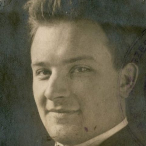 Portrait en noir et blanc d'un jeune homme aux cheveux courts, en costume et cravate. On aperçoit un tampon partiel sur la droite.