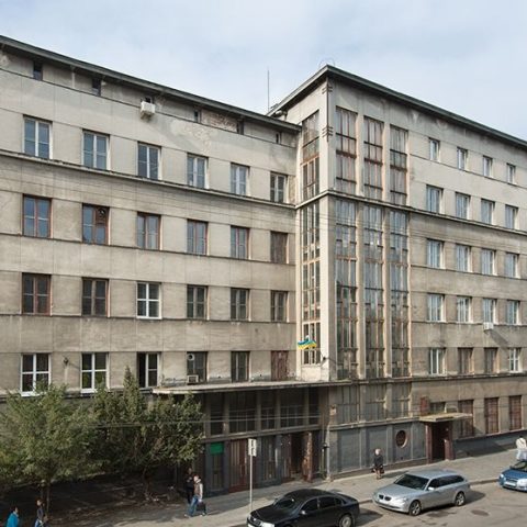 Bâtiment moderniste de l'Institution d'Assurance Sociale sur la rue Zelenia à Lviv, avec des bandes verticales de fenêtres et une baie vitrée semi-circulaire, surmonté d'une corniche massive.
