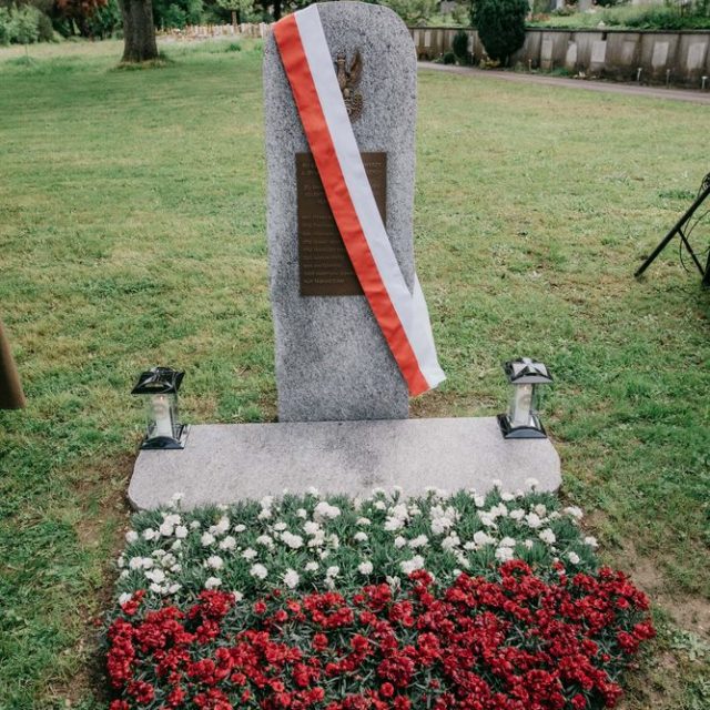 Obélisque en granit avec plaque en bronze et aigle polonais, drapé d'un ruban rouge et blanc, entouré de fleurs rouges et blanches au cimetière de Madretsch.