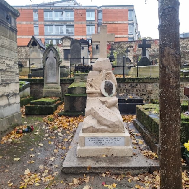 Tombstone of Juliusz Słowacki at Montmartre Cemetery in Paris, featuring a stone structure with a bronze medallion of the poet's likeness, a lyre, and stone books with inscriptions.