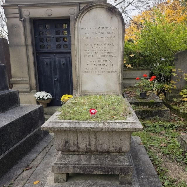 Tombe de Henryka et Ludwik Wołowski et Laura Guérin avec base en gradins, jardinière en forme de cercueil et stèle verticale avec croix. Fleurs et verdure entourent la tombe.
