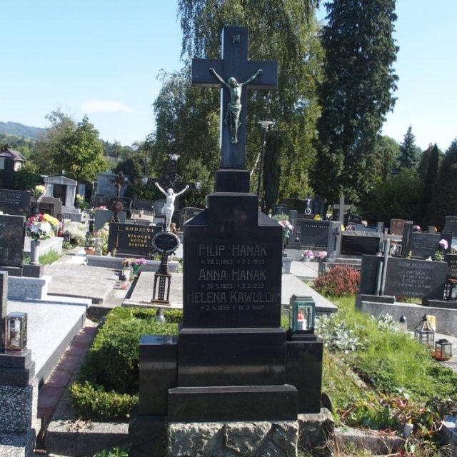 Надгробок Анни Ганак, Філіпа Ганака та Гелени Кавулок з хрестом на трирівневому постаменті. Хрест із фігурою Христа та написом 'REX VIDE CREATOR'. Постамент з гравірованими написами, з боків металеві ліхтарі.