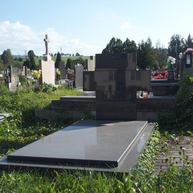Могила, позначена надгробною плитою з хрестоподібною стелою на голові, що складається з трьох менших плит. На стелі вигравірувано напис.