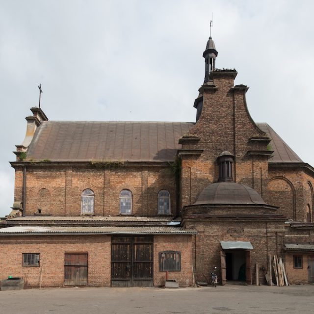 Цегляна церква в Світарзові з похилим дахом і арковими вікнами, з центральним куполом і хрестом на даху. Фасад має ознаки зносу.