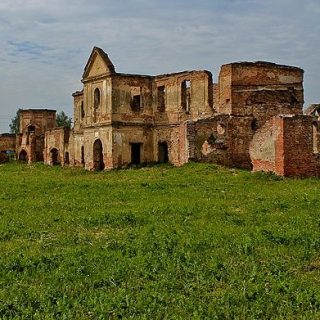 Ruiny klasztoru kartuzów w Berezie z częściowo stojącymi ceglanymi murami i pozostałościami fasady kościoła, otoczone trawą.