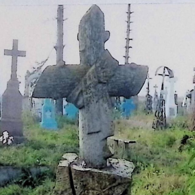 Могила, позначена хрестом, стилізованим під стовбур дерева, з стрічкою, перекинутою на перетині рамен. Основа і постамент нагадують стовбур дерева. Спереду прикріплена табличка з написом.