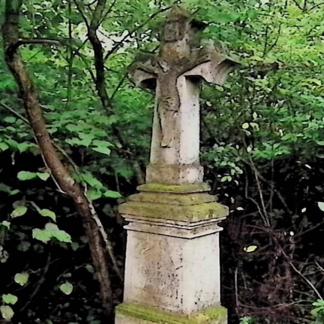 Tombe de Maria et Piotr Hreczyński avec une croix sur un piédestal à trois niveaux dans une zone boisée. La croix présente un relief du Christ à l'intersection de ses bras.