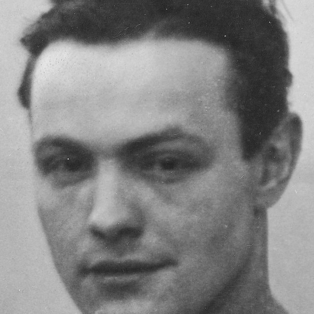 Black and white portrait of a man with short dark hair, looking directly at the camera.