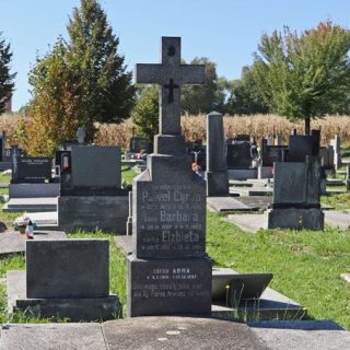 Nagrobek Anny, Barbary, Elżbiety i Pawła Cyran z krzyżem na dwustopniowym cokole. Krzyż ma mały metalowy krzyżyk na przecięciu ramion i zwój INRI powyżej. Grób otoczony innymi nagrobkami.