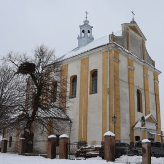 The Church of St. Stanislaus and St. Christopher in Hussaków, a brick building with a single-story facade and decorative gable, surrounded by snow-covered trees and a fence.
