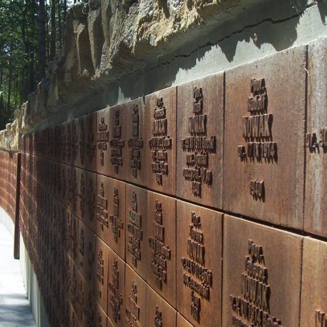 Un mur du souvenir sur lequel sont gravés les noms des victimes, situé dans la forêt de Katyn, entouré d'arbres.