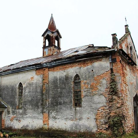 L'église paroissiale de la Sainte Famille à Majdan, Ukraine, montrant une structure en brique et plâtre en détérioration. Le bâtiment a des fenêtres cintrées, un toit endommagé et un petit clocher.