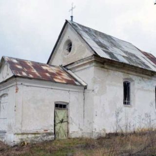 Église de la Visitation de la Bienheureuse Vierge Marie à Niżborg Nowy, Ukraine, avec une façade usée, un pignon triangulaire, une fenêtre circulaire et un toit rouillé. Une croix surmonte le pignon.