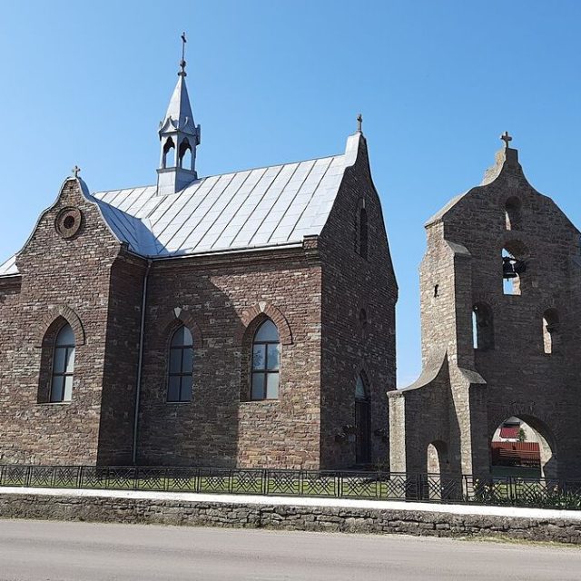 Église de l'Assomption de la Bienheureuse Vierge Marie à Rydoduby, Ukraine. Le bâtiment en pierre présente un plan en croix latine avec des fenêtres en arc brisé et un clocher. Un toit en métal et une flèche surmontée d'une croix sont visibles.