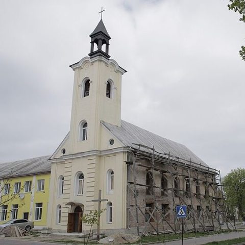 Église paroissiale Saint-Laurent à Chyrów, Ukraine. Le bâtiment présente une façade à trois axes avec une tour carrée et des fenêtres cintrées. Des échafaudages sont visibles sur le côté, indiquant des rénovations en cours.