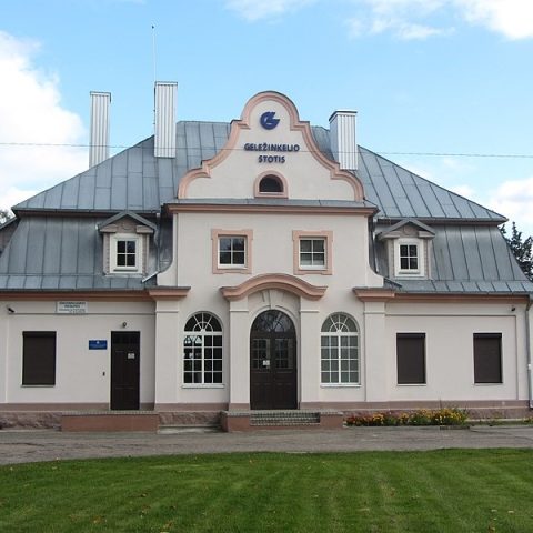 The railway station building in Rudziszki, with a mansard roof and neoclassical features, featuring a central entrance with an arched window and decorative details on the façade.