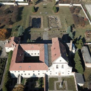 Vue aérienne de l'ancien monastère des Capucins à Olesko, montrant le bâtiment principal avec une cour, entouré de jardins et d'étangs. Le site est en cours de travaux de conservation.