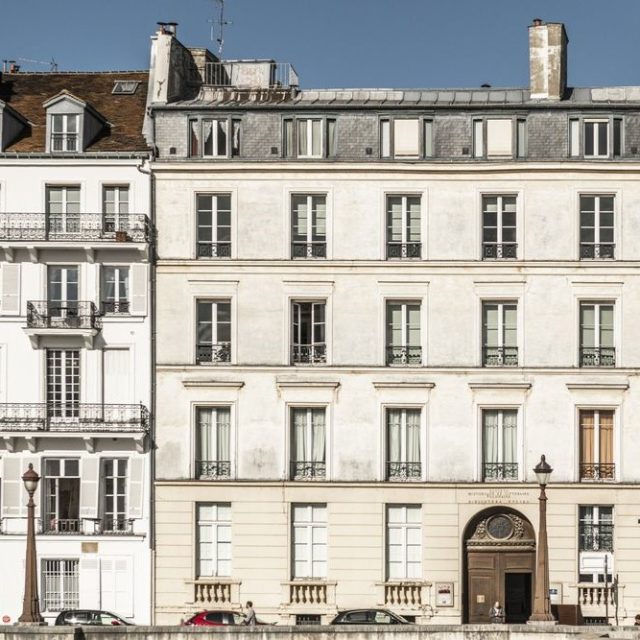 Une photographie de la façade avant du bâtiment de la Bibliothèque polonaise à Paris, avec ses rangées de fenêtres, son toit mansardé et son entrée voûtée sur le quai d’Orléans.