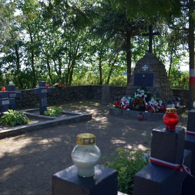 Cimetière des soldats de l'Armée nationale, avec un monument en pierre, des croix et des bougies allumées, entouré d'arbres.