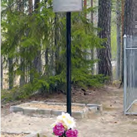 Une croix en métal avec une plaque au cimetière forestier des exilés polonais en Kargovine. Des fleurs et des bougies rouges se trouvent à la base de la croix.