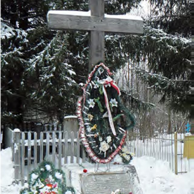 Krzyż pamiątkowy na zaśnieżonym cmentarzu w Zaowrażu, upamiętniający Polaków i innych więźniów zmarłych w łagrach kotłaskich. Podstawa z tablicą z inskrypcjami, ozdobiona wieńcami i świecami.