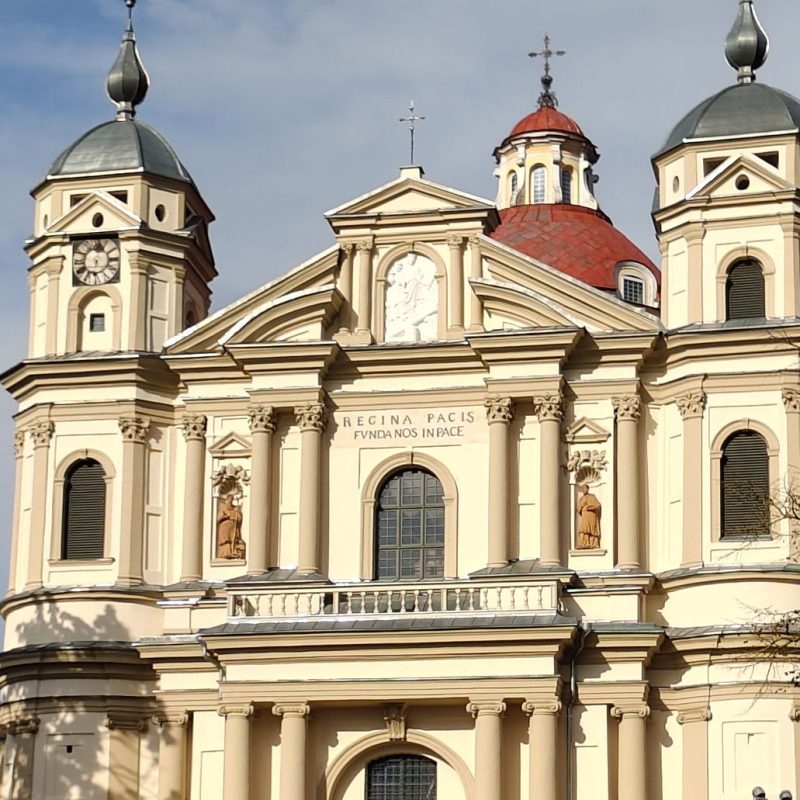 Façade de l'église Saint-Pierre-et-Saint-Paul à Antakalnis, Vilnius, avec deux tours à dômes, un fronton central avec l'inscription 'REGINA PACIS FUNDA NOS IN PACE', et des statues dans des niches.