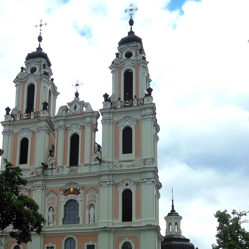 Fasada kościoła benedyktynek św. Katarzyny w Wilnie z dwiema pięciokondygnacyjnymi wieżami i elementami dekoracyjnymi. Widoczne są posągi i detale architektoniczne na tle pochmurnego nieba.