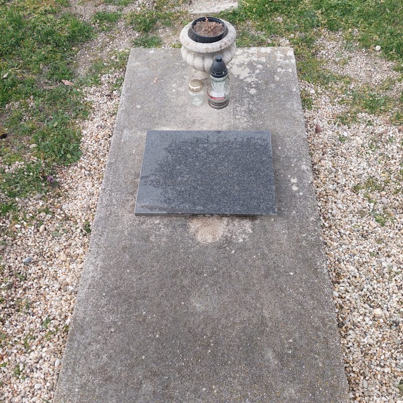 The grave of the Polish soldier Piotr Żak, with a granite slab bearing his name and the dates 1911–1942. On the concrete slab there are two candles and a flowerpot.