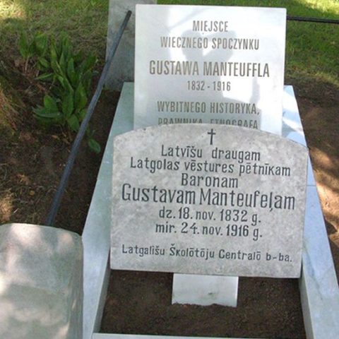 Могила Густава Мантеуффа на кладовищі в Дрицанах. Дві надгробні плити з написами польською та латвійською мовами. Польський текст вшановує Мантеуффа як історика, юриста та етнографа. Оточена зеленню.