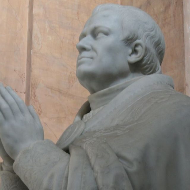 Marble sculpture of Pope Pius IX by Thomas Oskar Sosnowski in Rome, showing the Pope kneeling in prayer with a detailed cape and stole. The tiara stands on a plinth beside him.