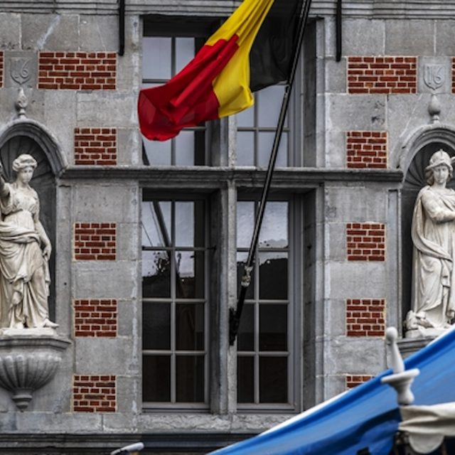 Sculptures de la Vérité et de la Justice sur la façade de l'ancien hôtel de ville à Halle, en marbre blanc, chacune dans une niche à côté d'une fenêtre. Un drapeau belge est visible au-dessus.