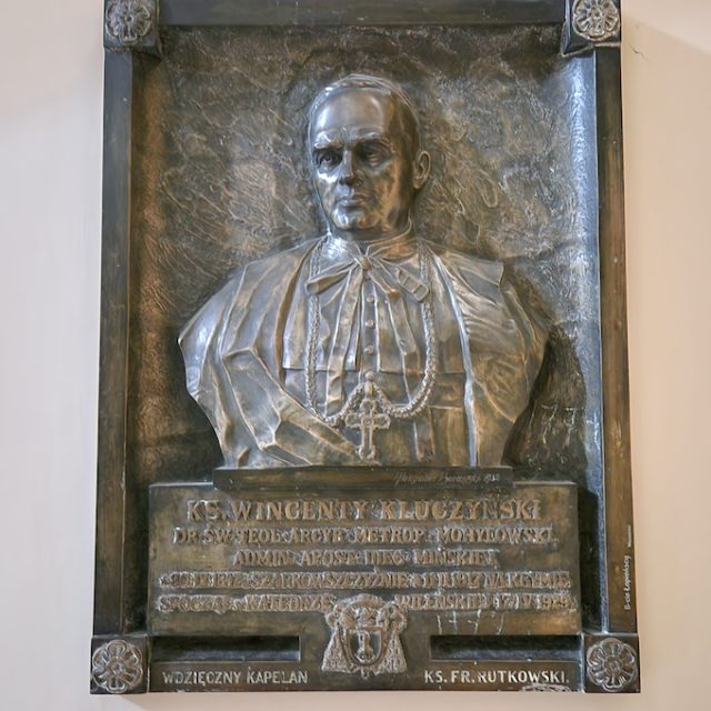Une plaque commémorative en bronze dédiée au père Wincenty Kluczyński, située dans la cathédrale de Vilnius, ornée d'un buste en bas-relief et d'une inscription, et placée dans la chapelle de l'Annonciation.