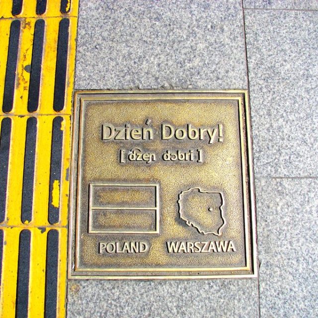 Bronze plaque embedded in the sidewalk with the inscription 'Dzień Dobry', the Polish flag, and a map of Poland with Warsaw marked. Located near Itaewon Station, Seoul.