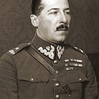 A portrait of a man in military uniform, wearing medals and insignia, seated against a background of patterned wallpaper.